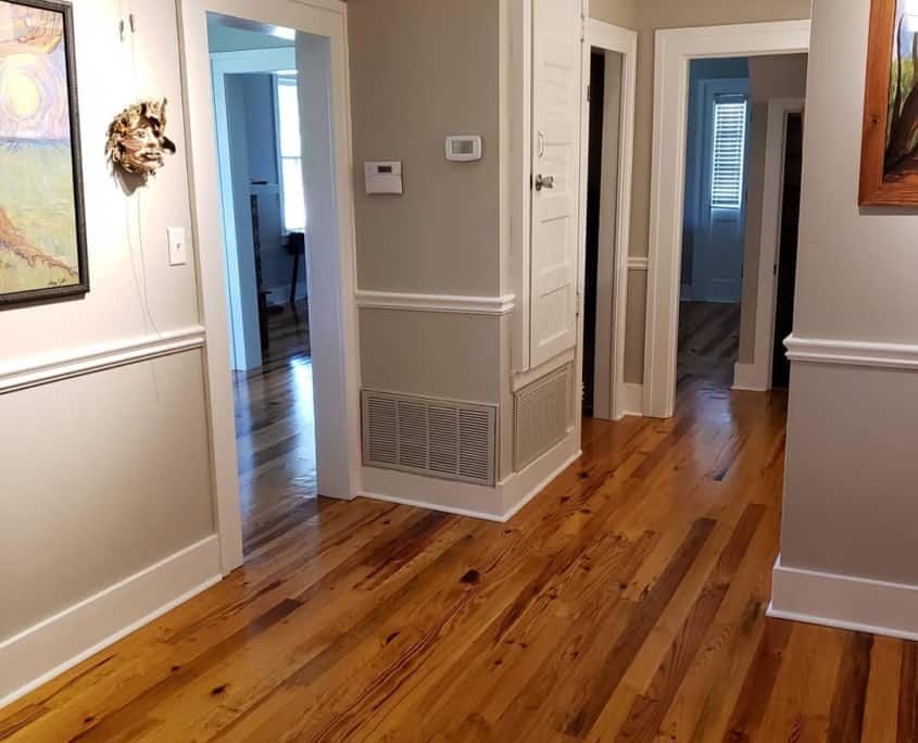 Hallway with wood floors, doorways, artwork, and a vent.