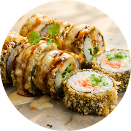 Sushi rolls topped with creamy sauce and garnish, arranged on a plate with dipping sauce.