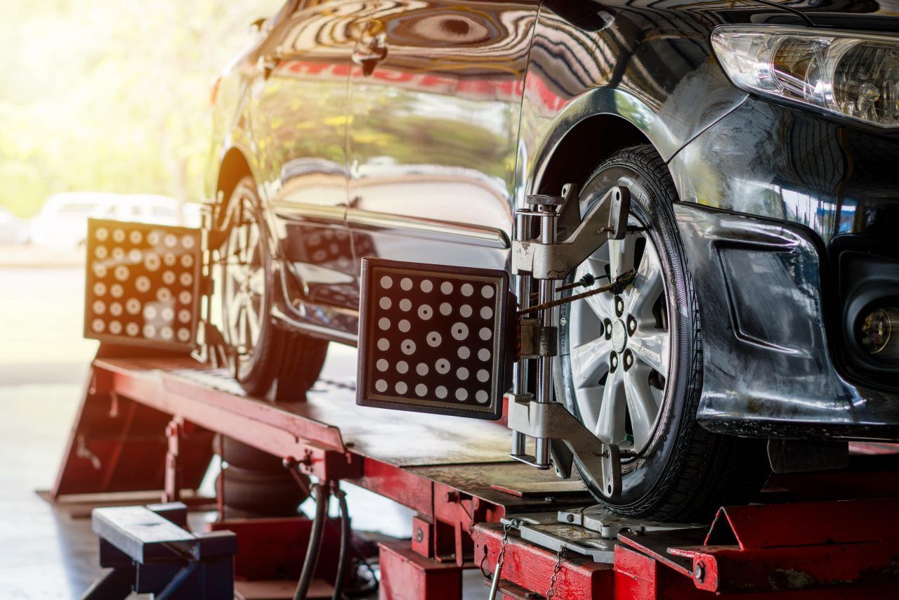 Car on a lift with alignment tools attached to the wheels in a repair shop.