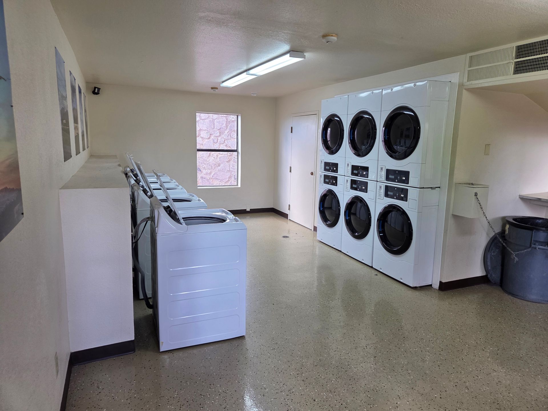 A clean, brightly lit laundry room with a row of white washing machines and several stacked white clothes dryers.