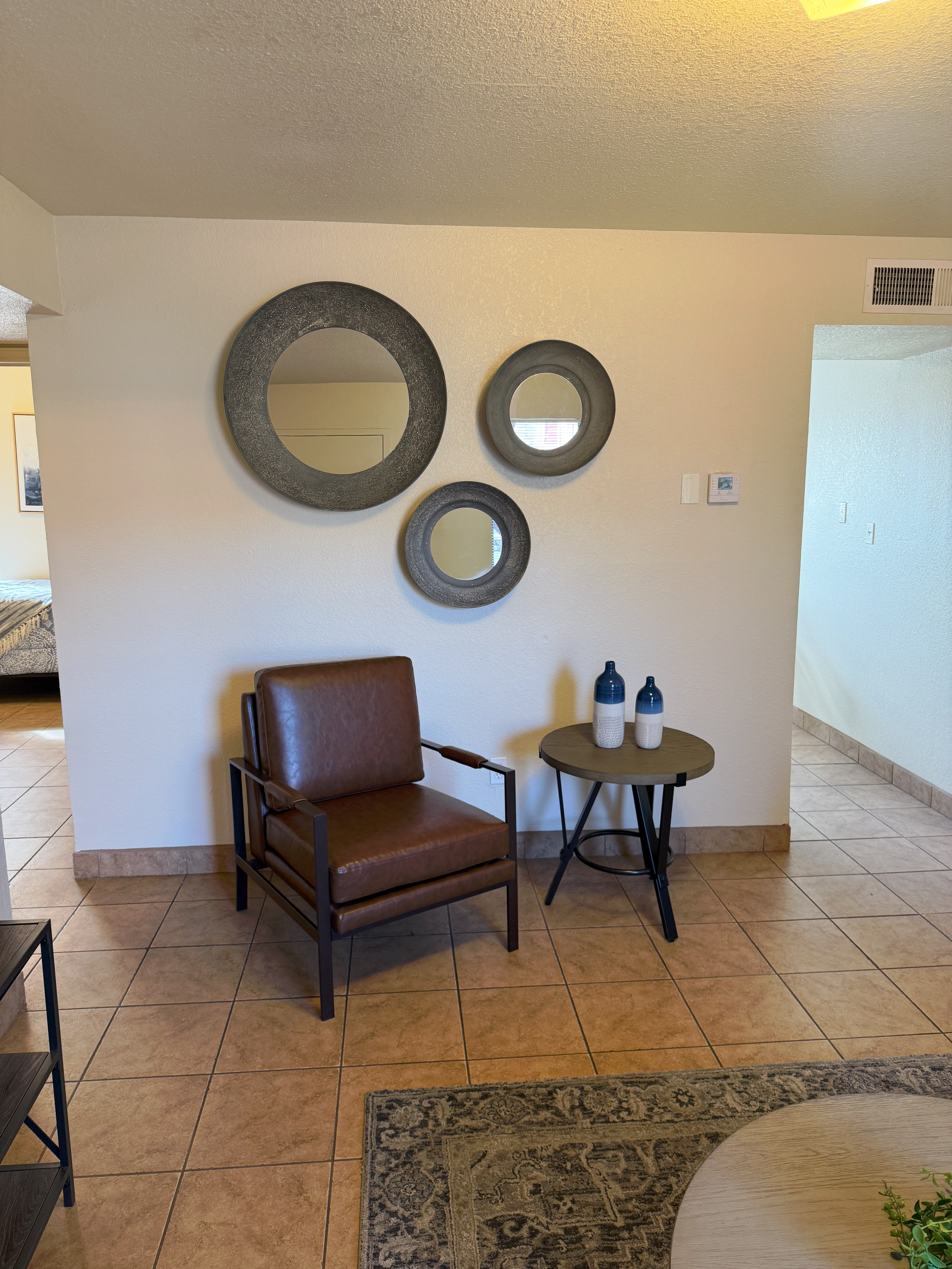 A brown leather armchair and a small round table with blue vases sit on tiled flooring below three circular wall mirrors.
