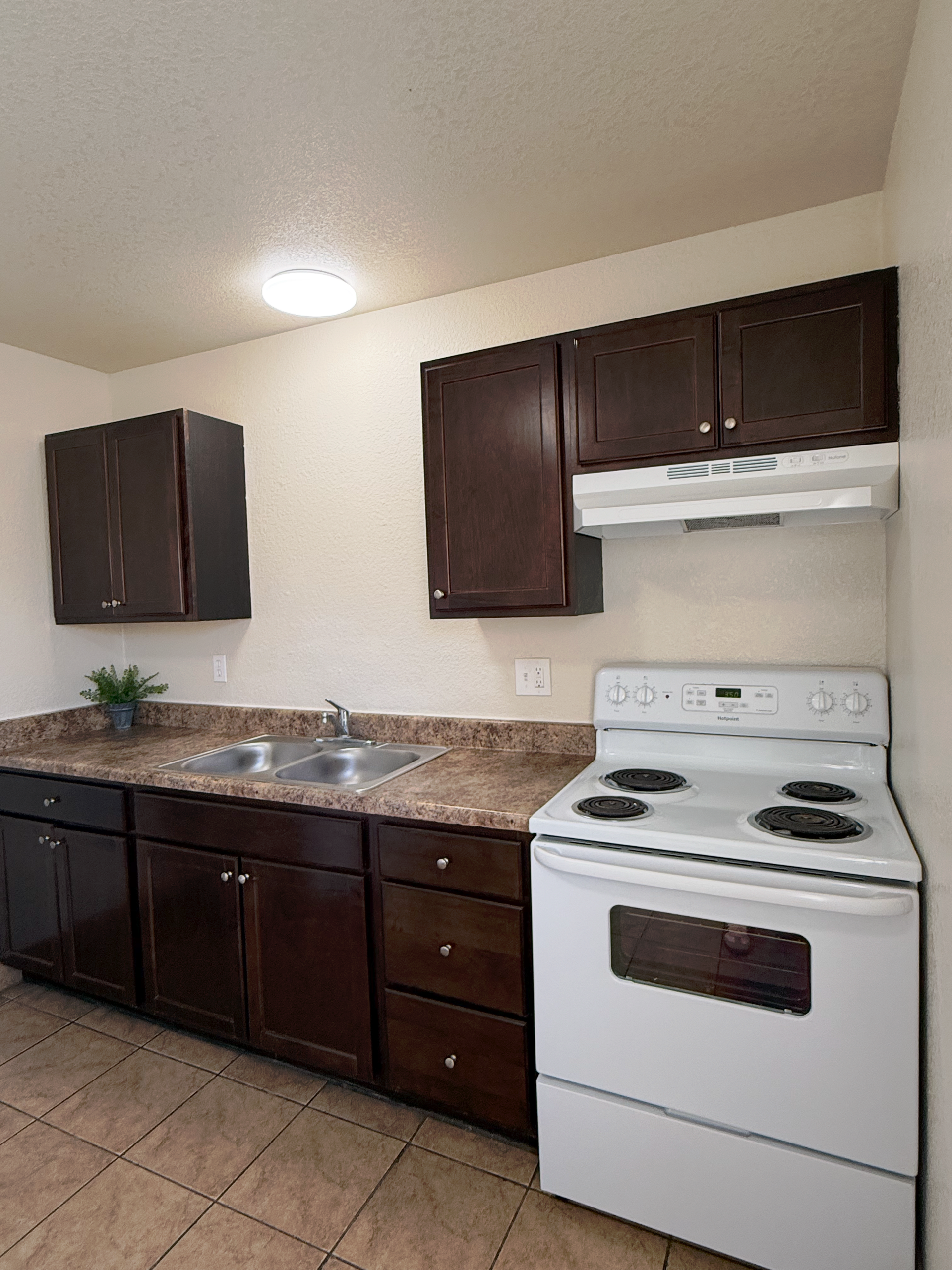 A kitchen featuring dark wood cabinets, a brown speckled countertop, a stainless steel sink, and a white electric stove.