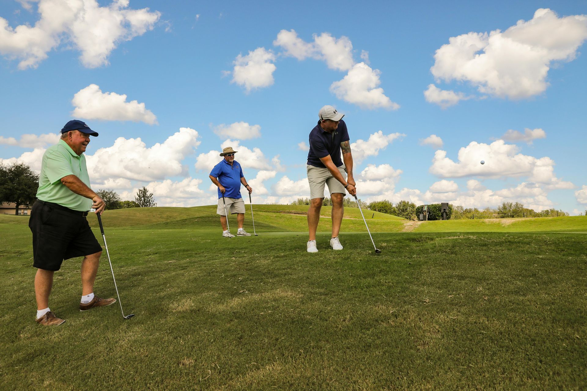 Man in white polo shirt and golf glove, holding a golf club on shoulder, looking away.