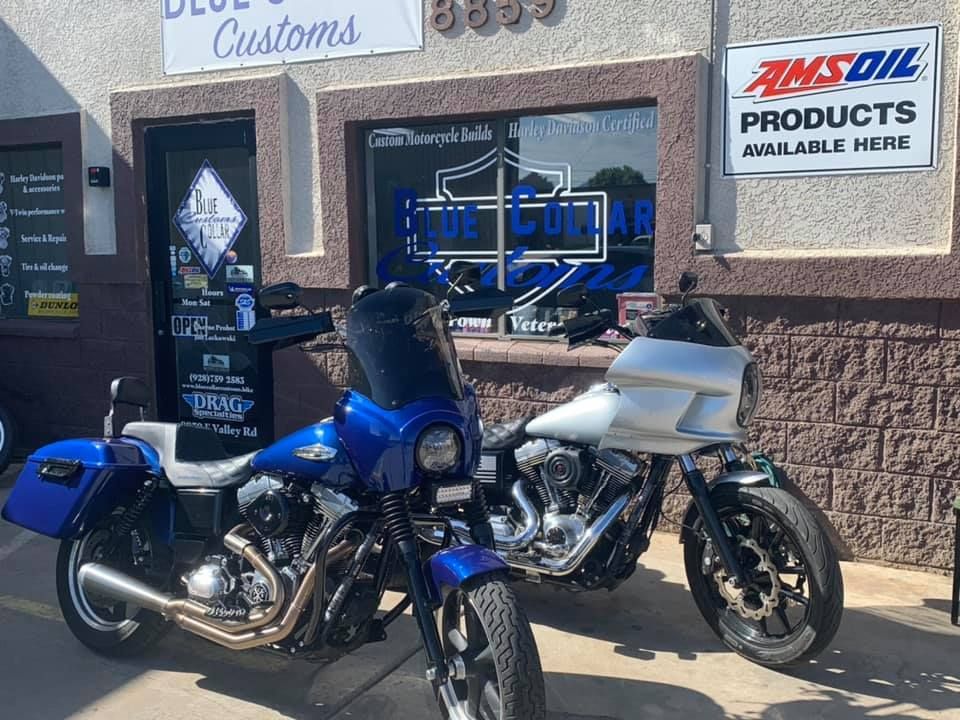 Two motorcycles parked in front of a shop named Blue Collar Customs, featuring blue and silver body paint.