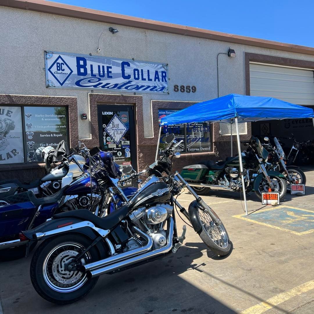 A motorcycle shop named Blue Collar Customs with several parked motorcycles, a blue canopy tent, and a sunny sky.