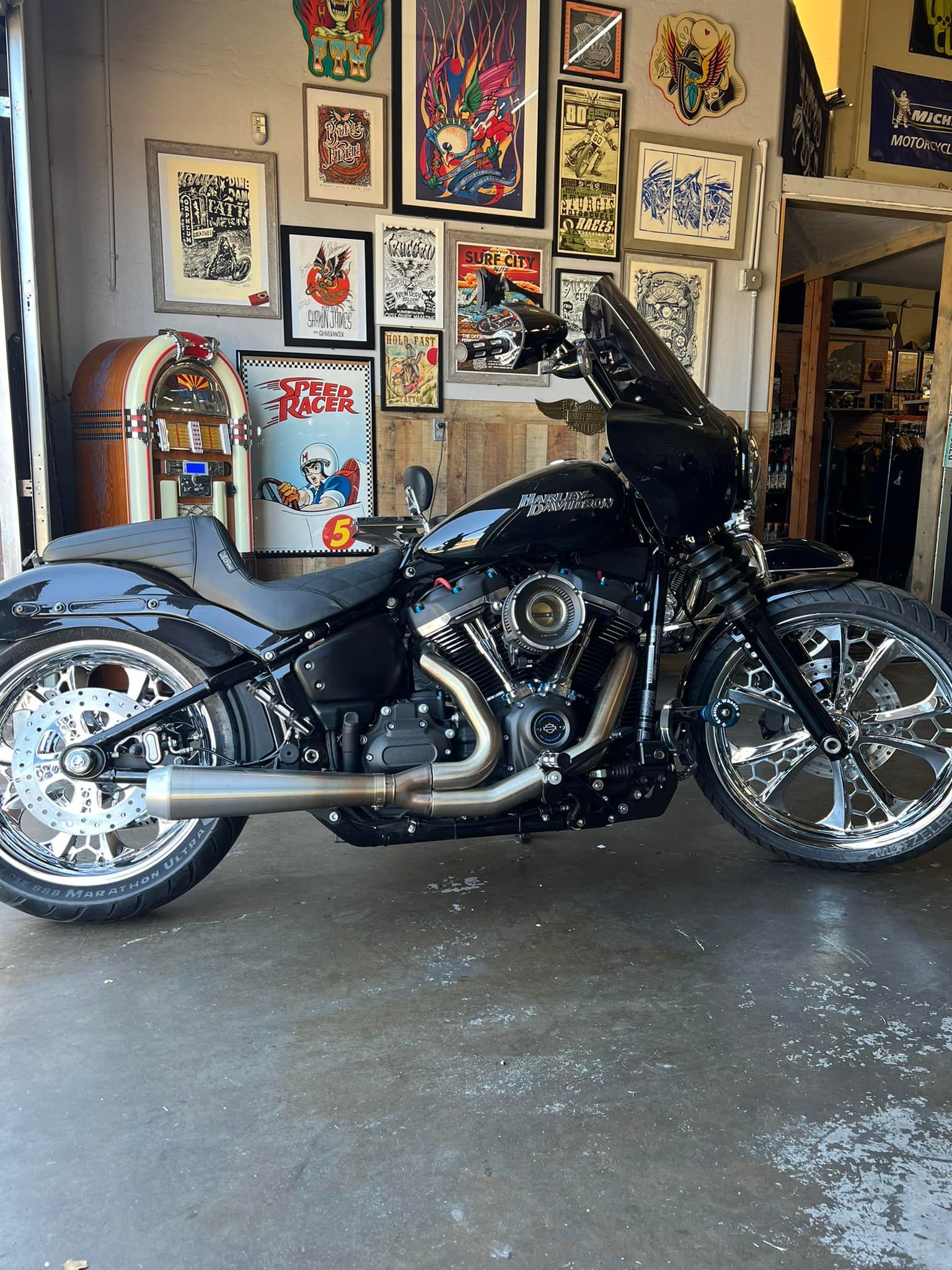 A black custom cruiser motorcycle with large chrome wheels parked in a garage decorated with numerous posters.