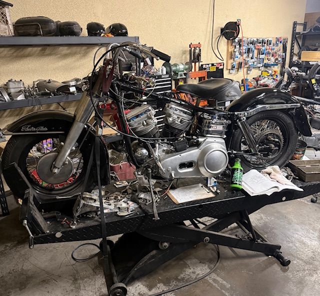 A vintage Harley-Davidson motorcycle being restored on a mechanical lift in a workshop filled with tools and parts.