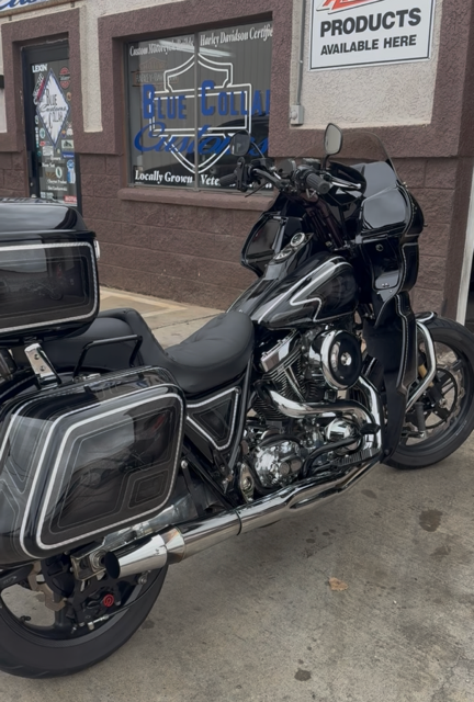 A black Harley-Davidson motorcycle with hard saddlebags parked on a sidewalk in front of a storefront.
