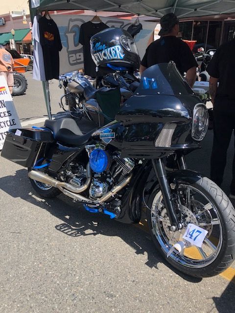 A black Harley-Davidson motorcycle with bright blue engine accents parked at an outdoor event on a sunny day.