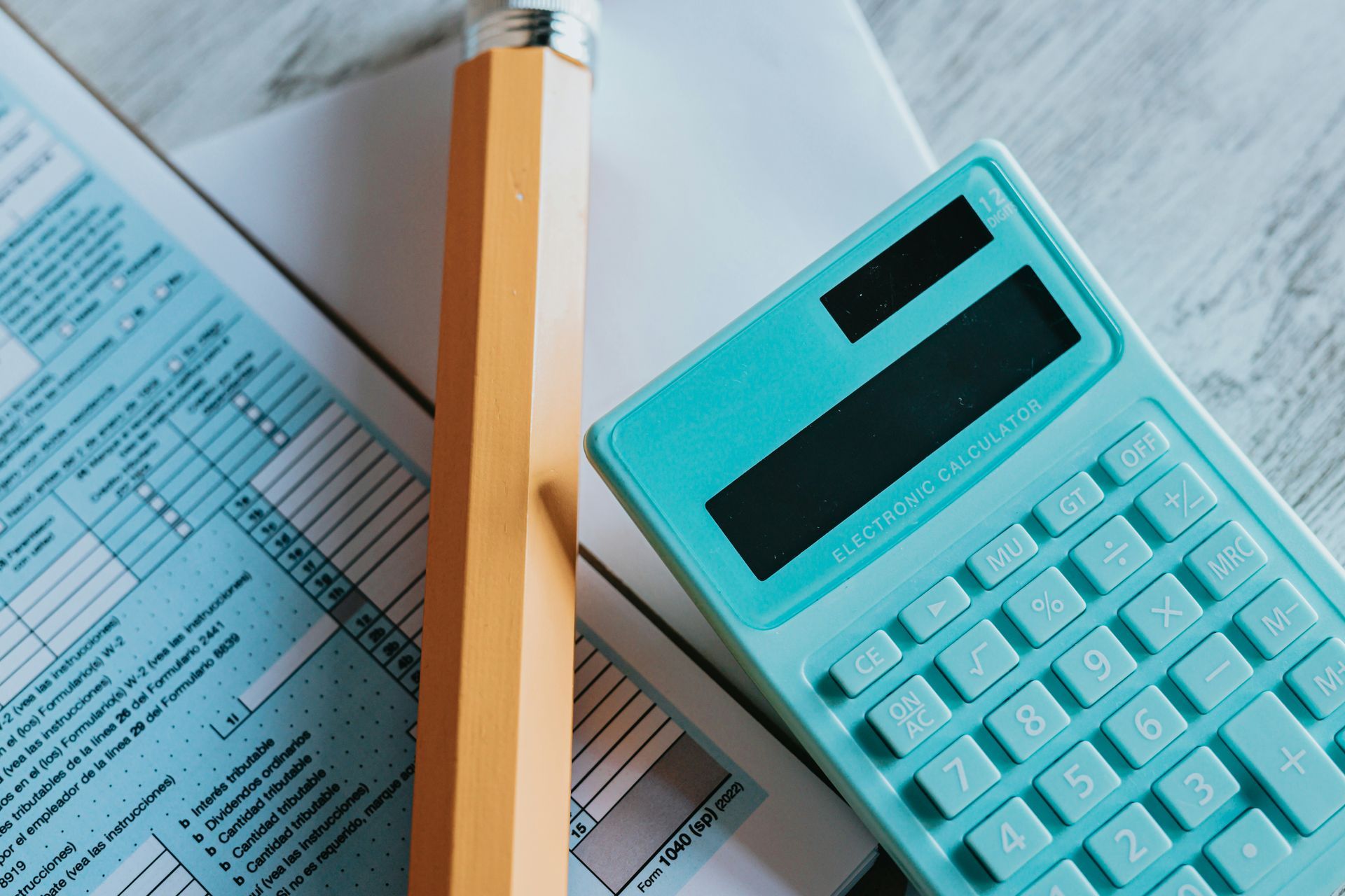 Blue calculator, tax form, and pencil on a light wooden surface.