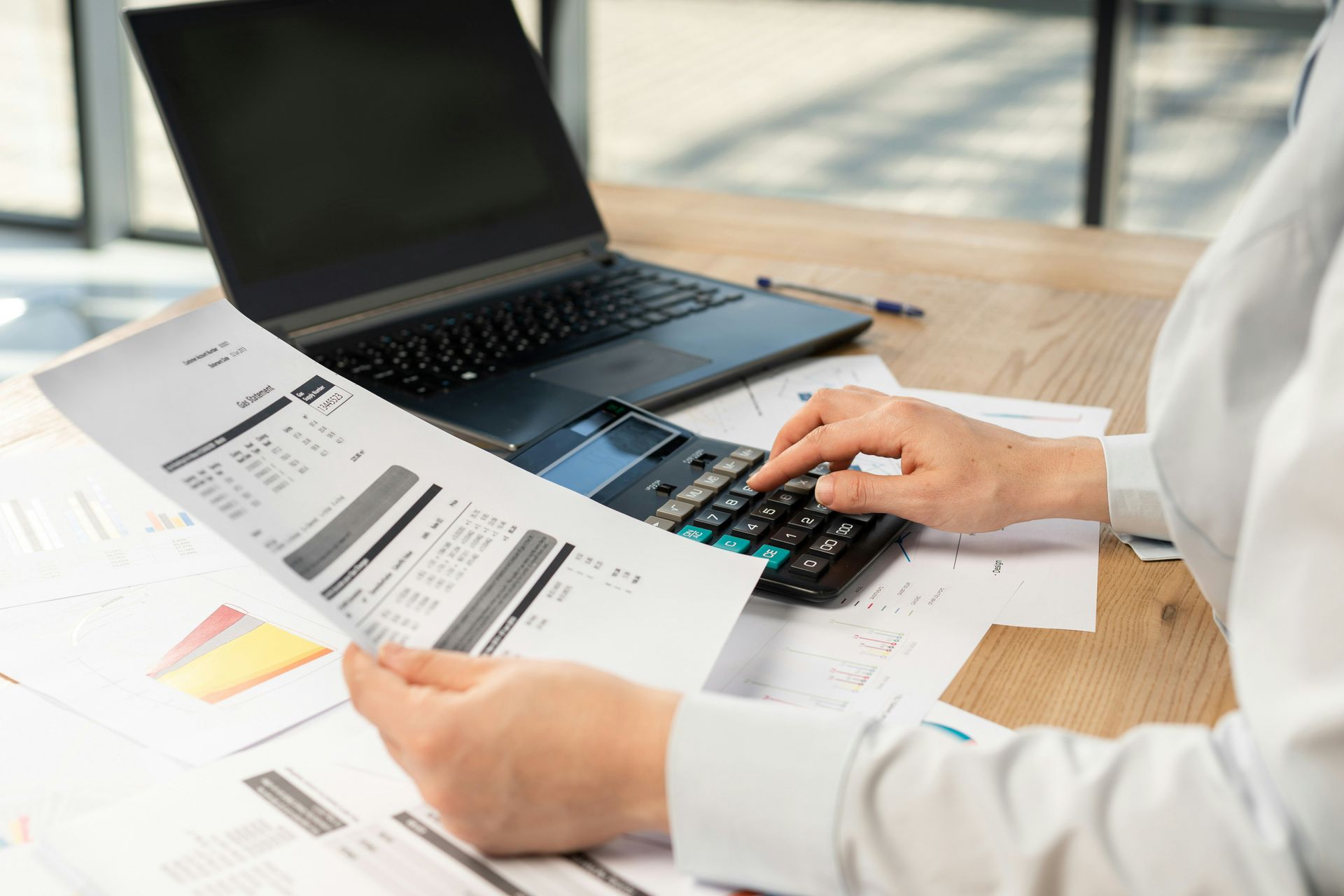 Person using a calculator while reviewing financial documents at a desk with a laptop.