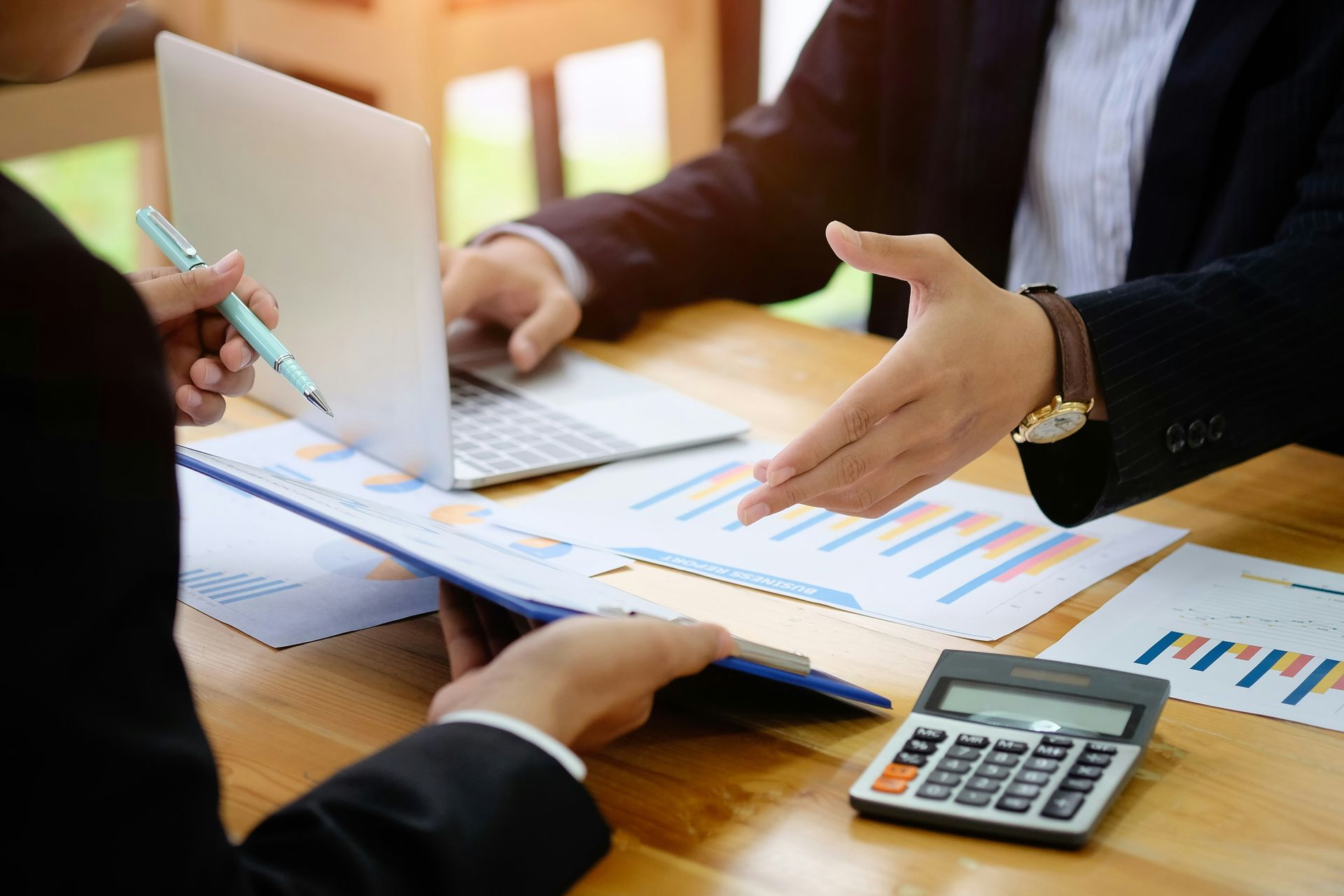 Two people in suits reviewing financial documents at a desk, one points with hand.