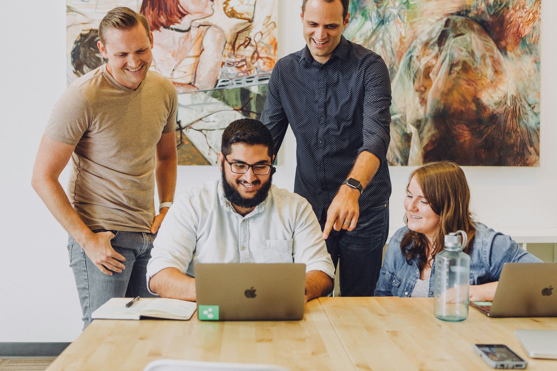 Four people collaborate around a laptop at a wooden table.