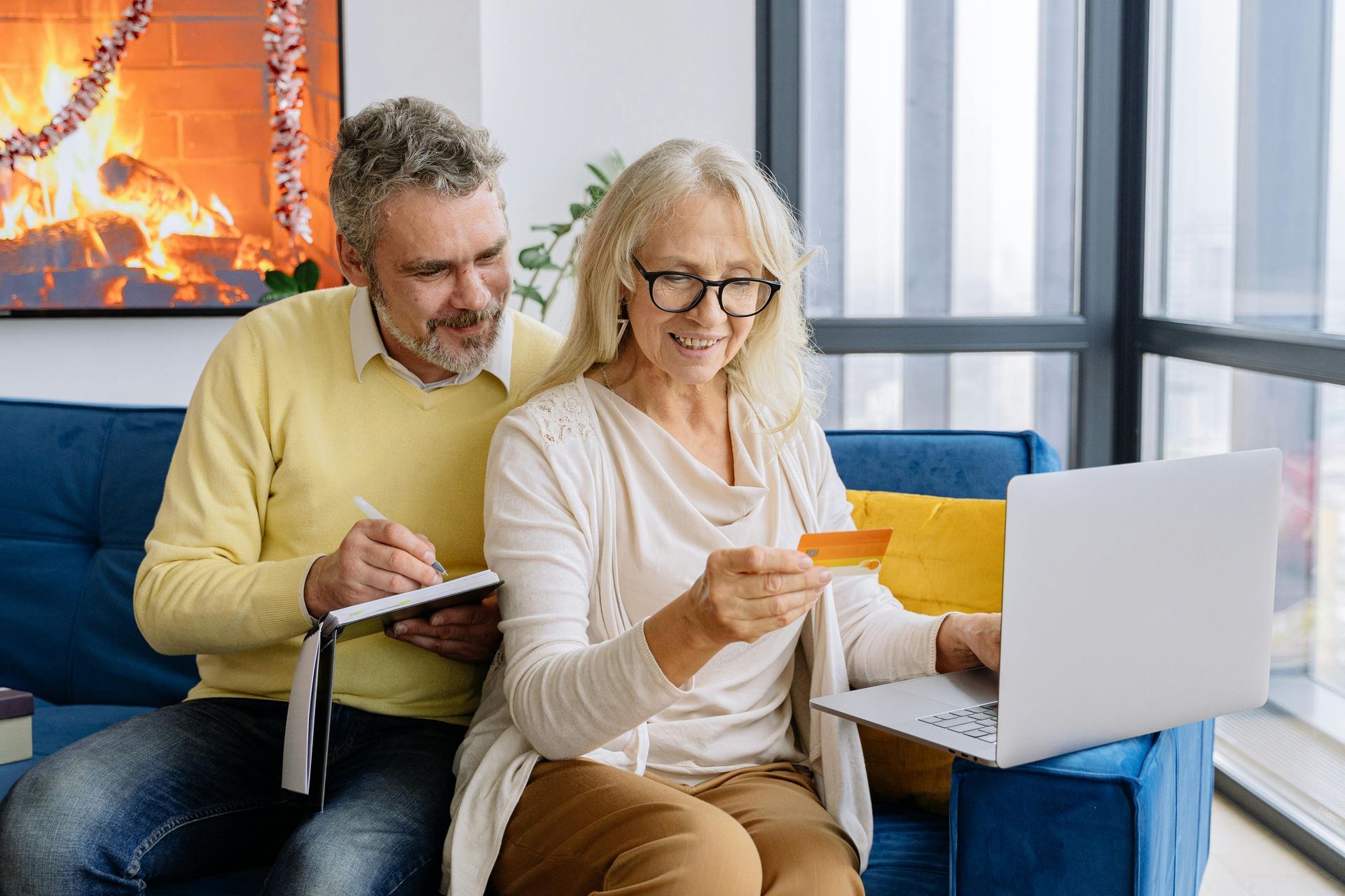 Couple on couch using laptop, woman holding credit card, man writing in notebook.