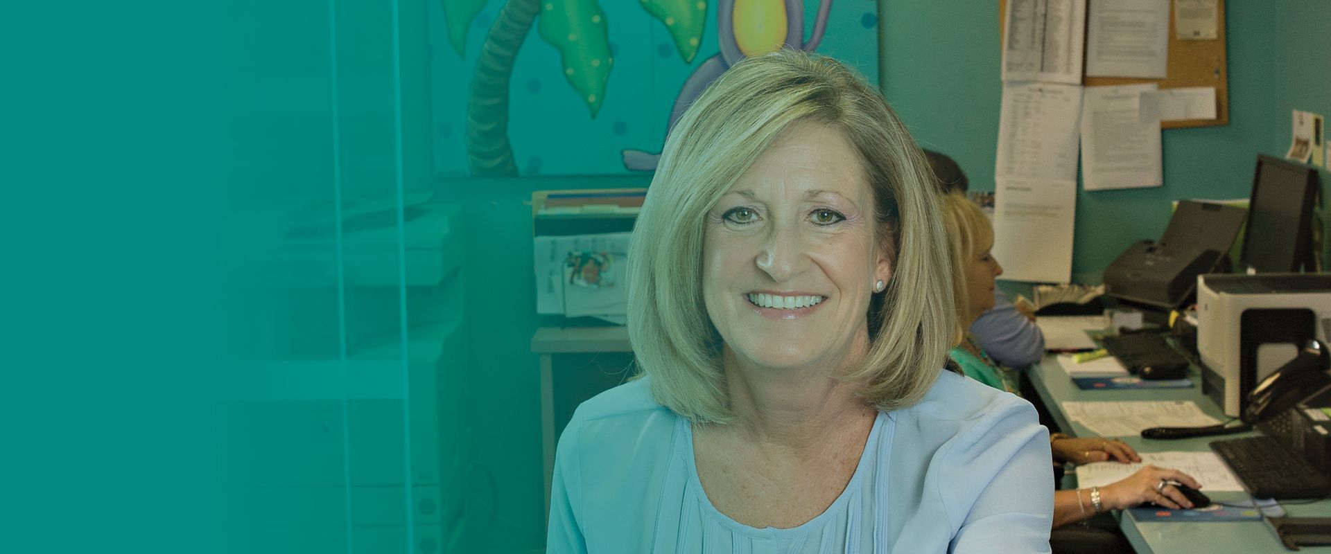 A woman is smiling while sitting at a desk in an office.