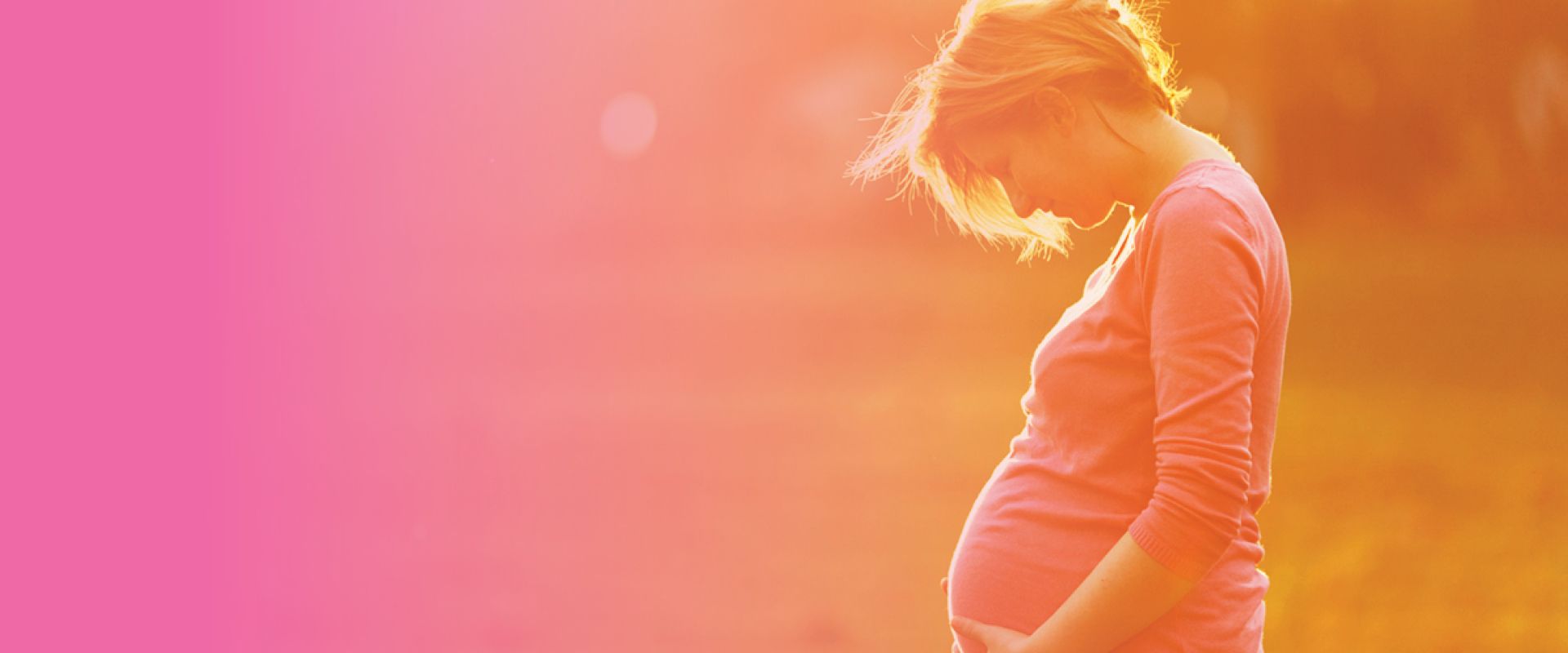 A pregnant woman in a pink shirt is holding her belly.