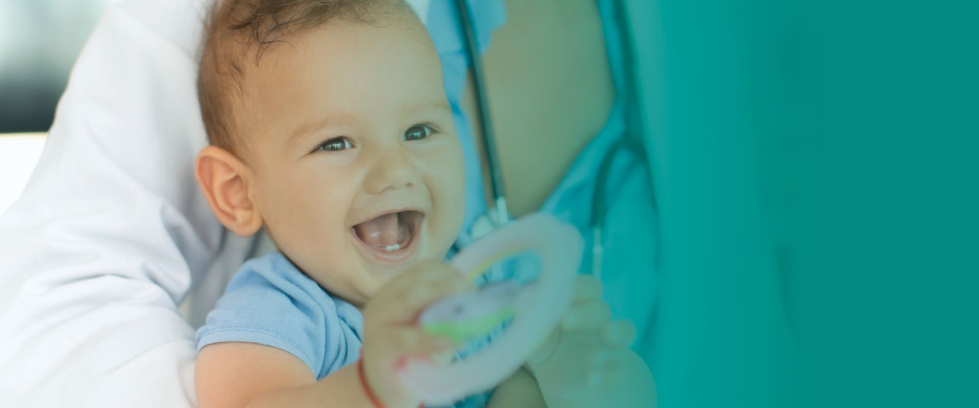 A baby is sitting on a bed holding a toy and smiling.