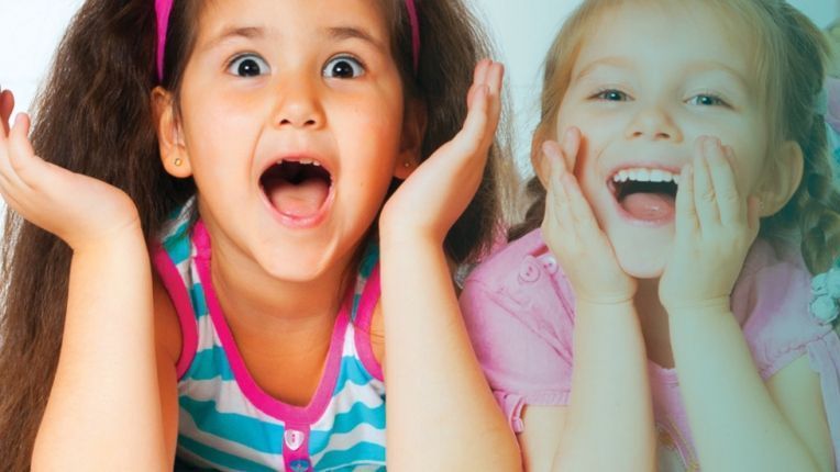 Two little girls are sitting next to each other with their mouths open.