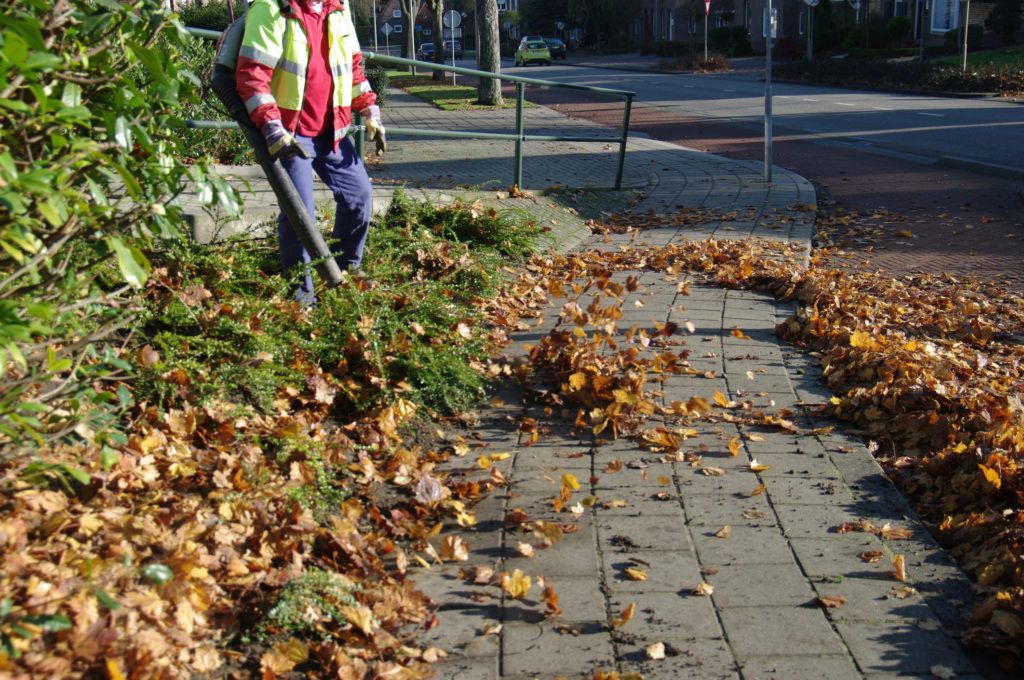 A man is blowing leaves on the sidewalk with a blower