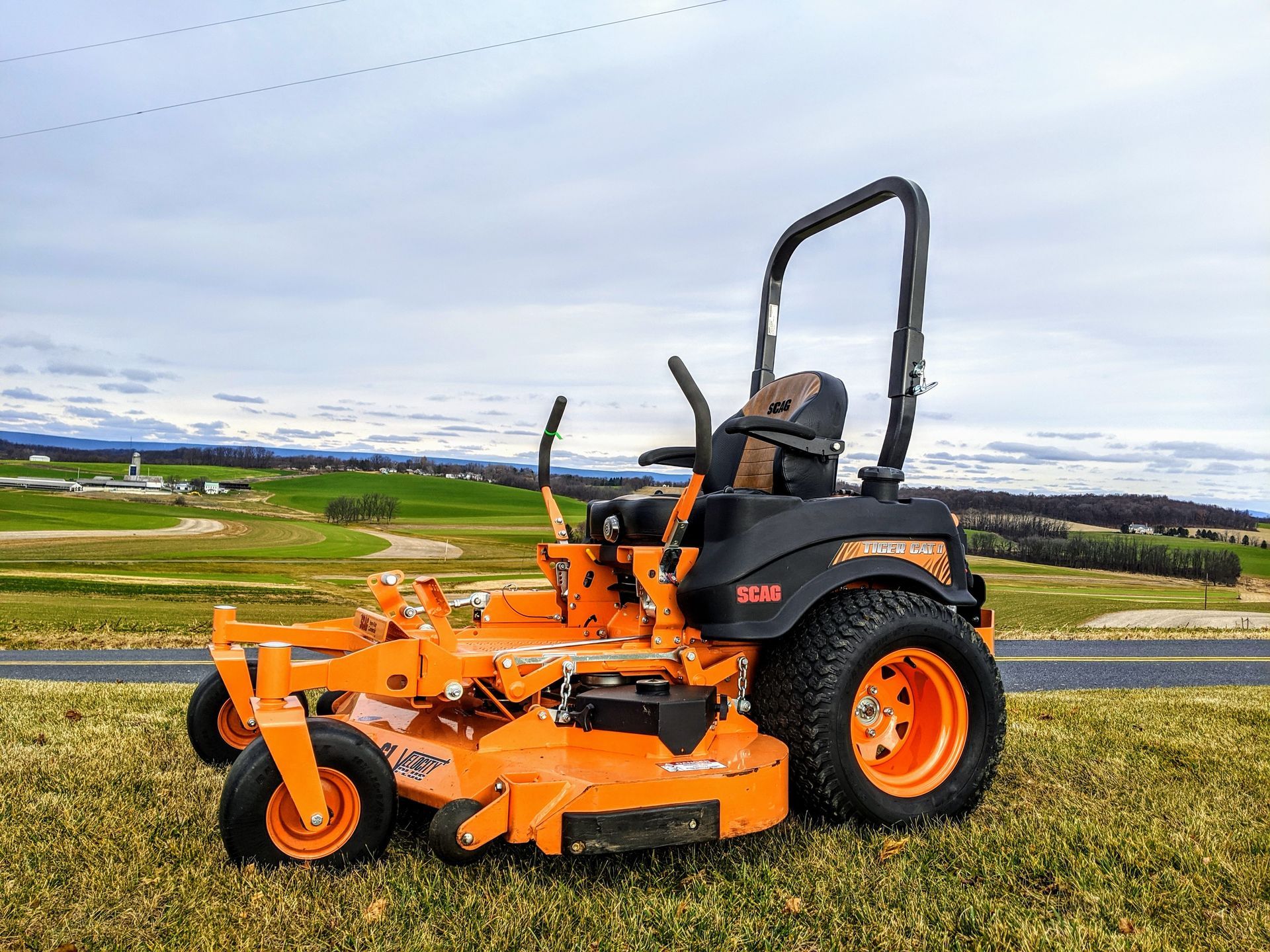 An orange and black lawn mower is parked on the side of the road.