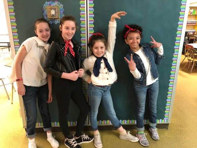 A group of young girls are posing for a picture in front of a bulletin board.