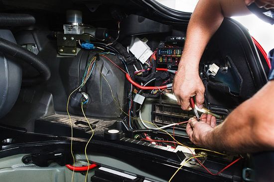 due mani di un elettrauto mentre sistema un impianto all’interno di una vettura e vista dei fili di diversi colori