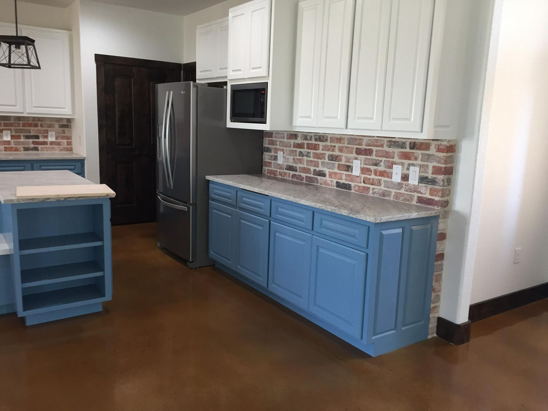 Blue and white kitchen with brick backsplash, stainless steel refrigerator, and wood floor.