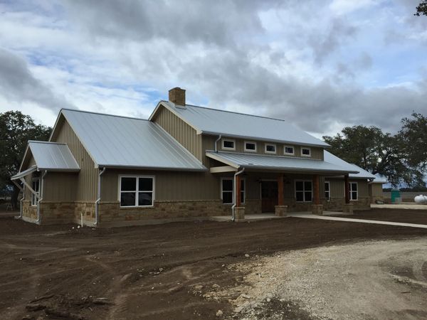 Tan and stone house with a metal roof and a cloudy sky.