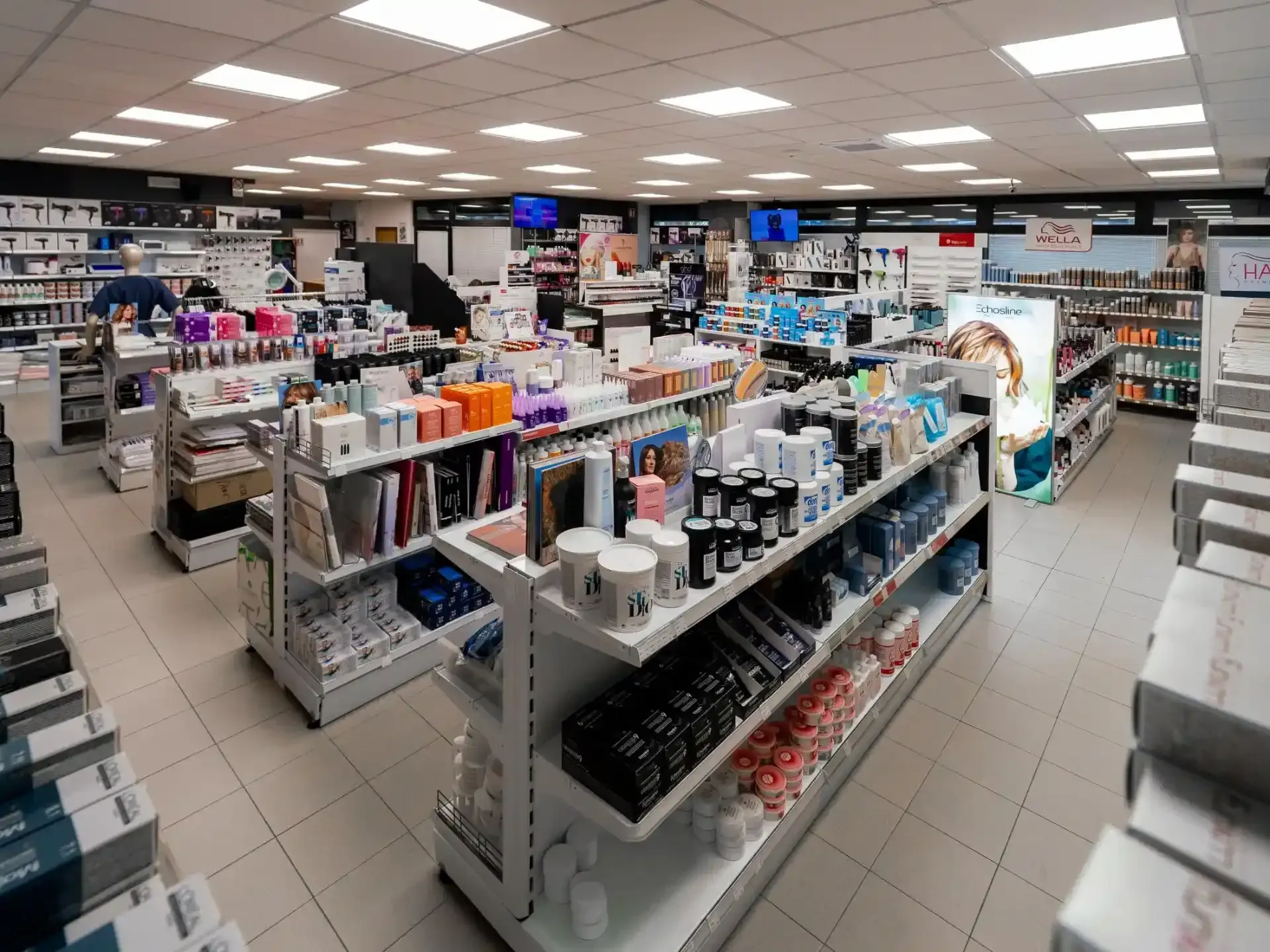 Interno della farmacia pieno di scaffali pieni di prodotti, illuminazione intensa dall'alto.