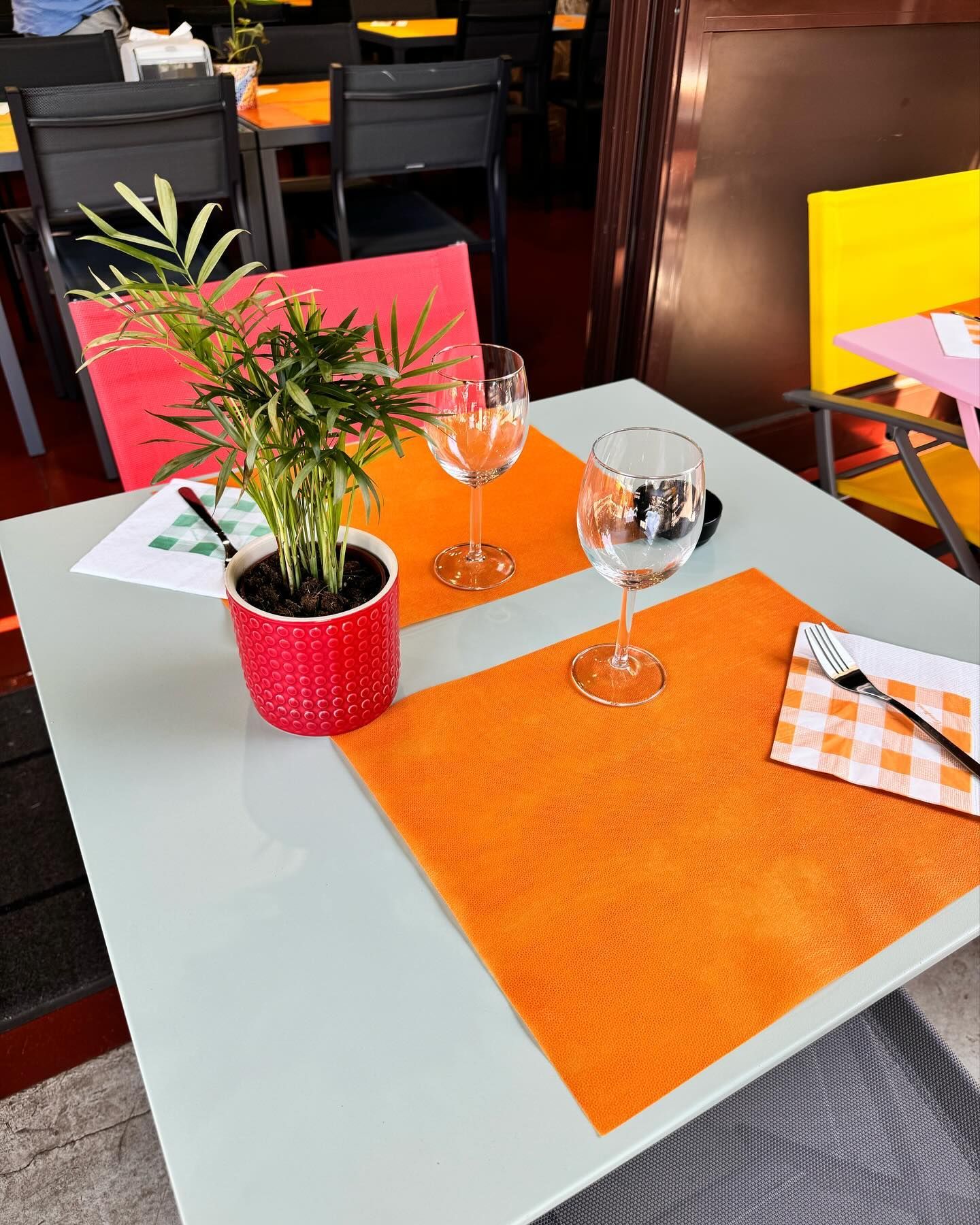 Un tavolo con sopra una pianta, bicchieri da vino e tovaglioli.