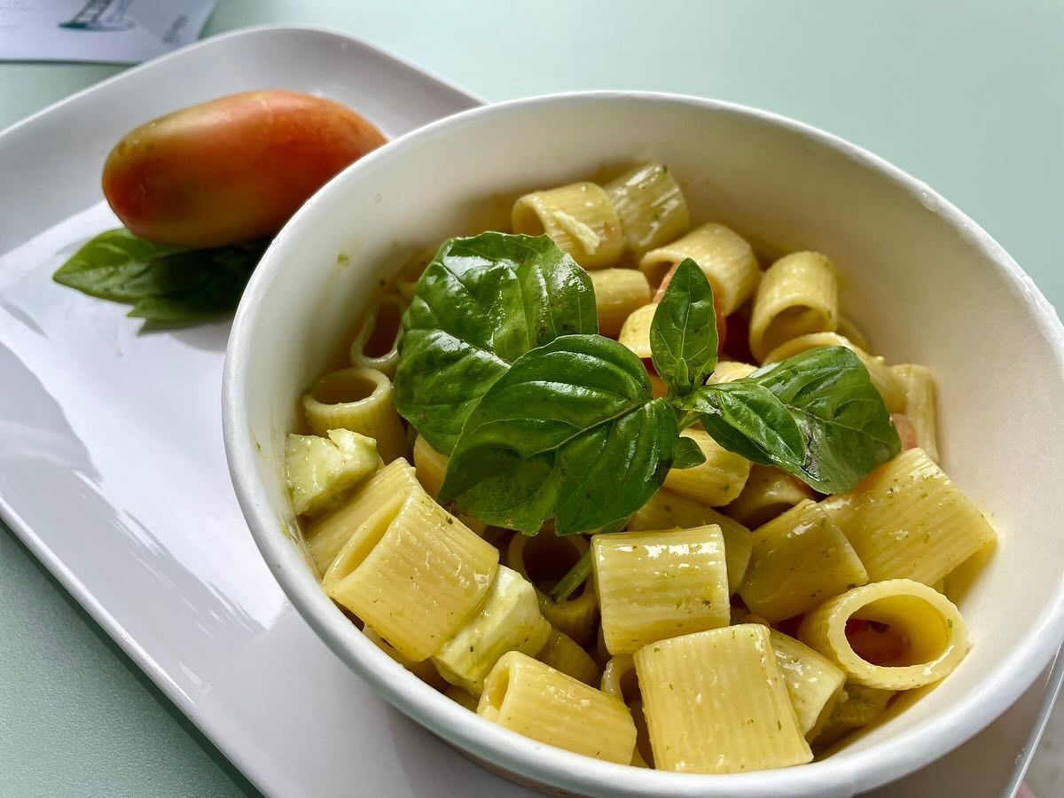 Una ciotola di pasta al basilico accanto a un pomodoro su un piatto