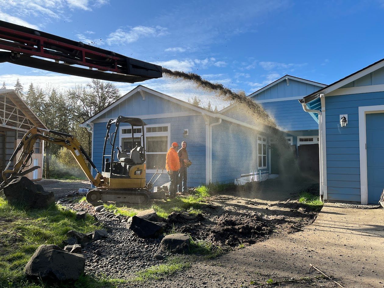 A man is standing in front of a house while a bulldozer is moving dirt in front of it.