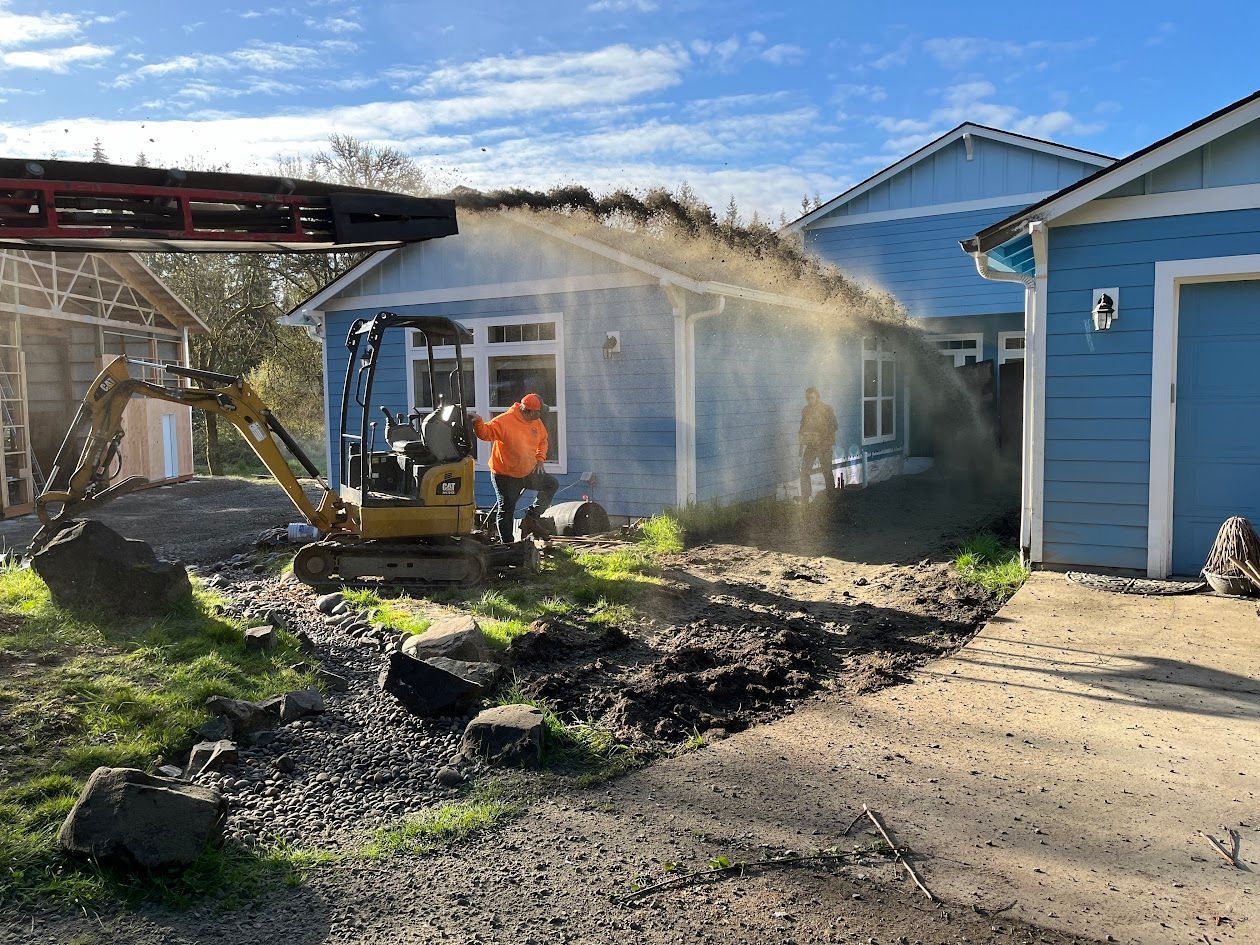 A man is driving an excavator in front of a blue house.