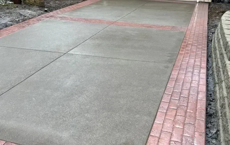 A concrete driveway with a red brick border.