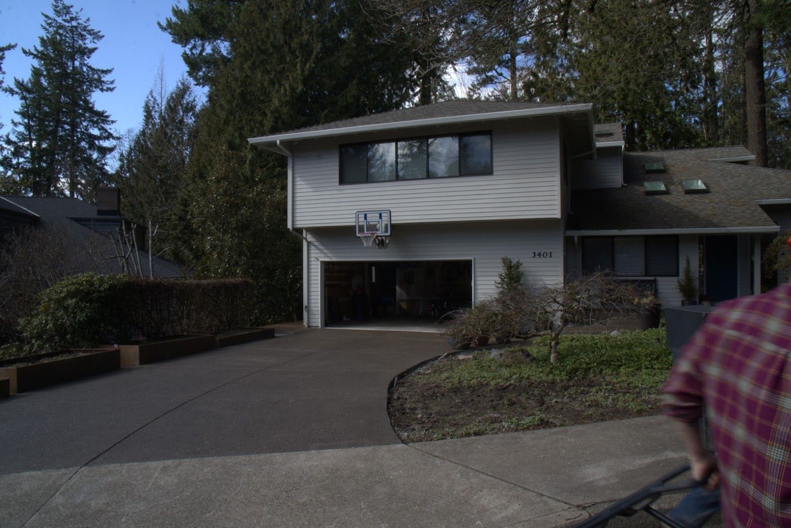 A man in a plaid shirt is pushing a stroller in front of a house.