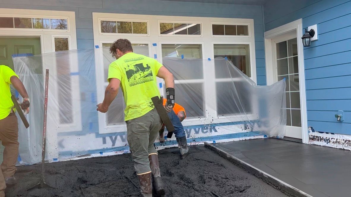 A group of men are working on a concrete floor in front of a house.
