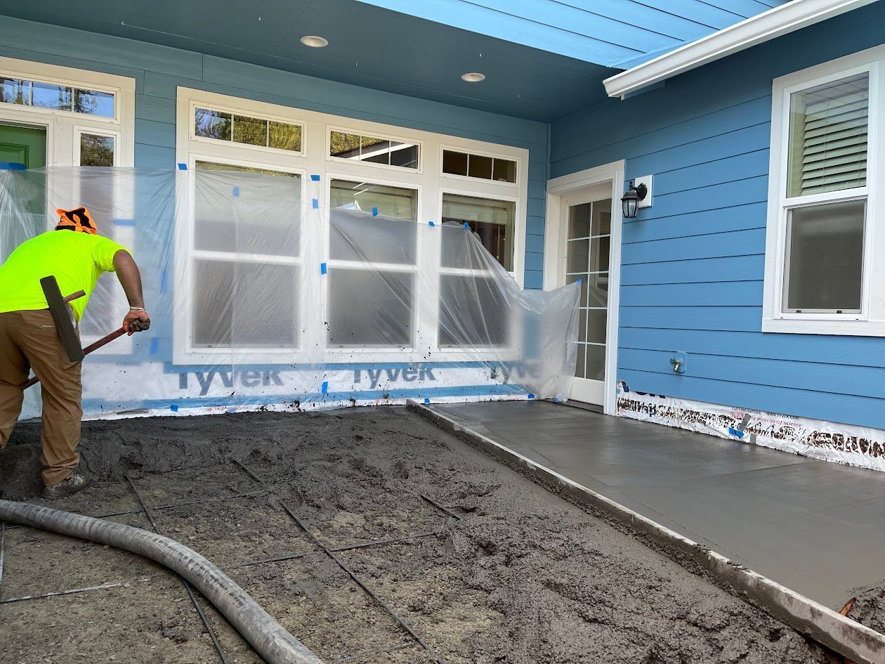 A man is working on a concrete walkway in front of a blue house.