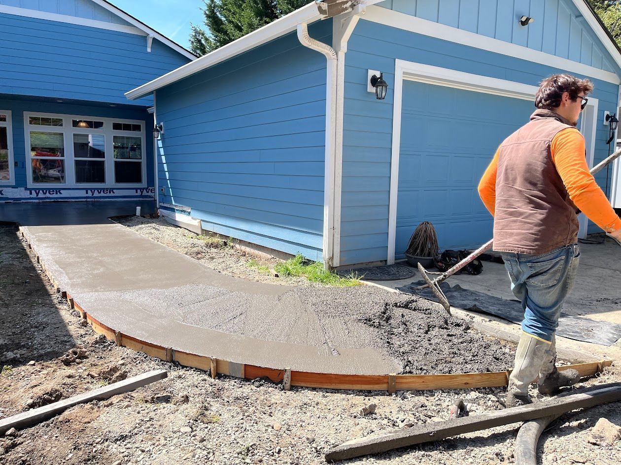 A man is shoveling concrete in front of a blue house.