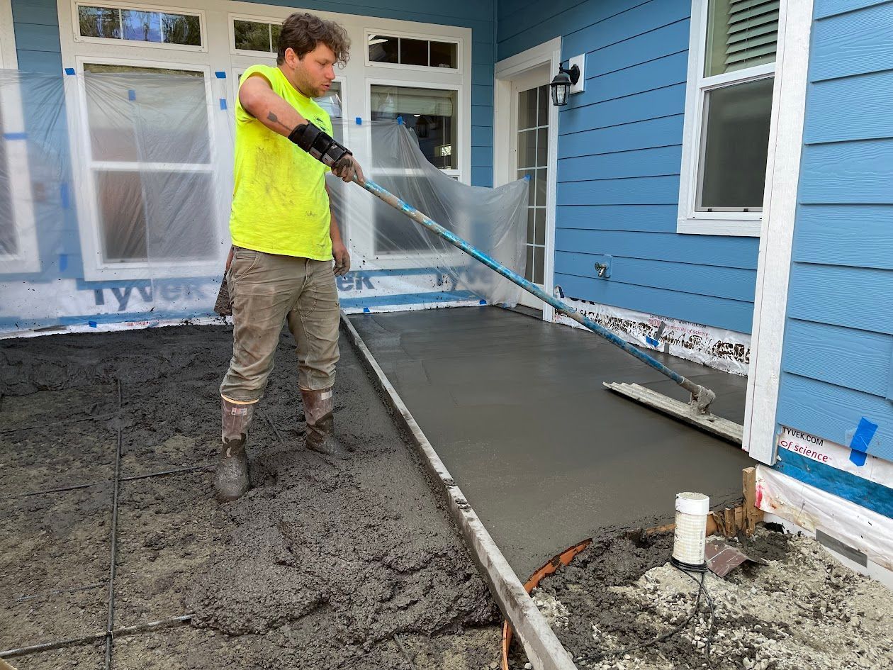 A man is spreading concrete on a sidewalk in front of a house.