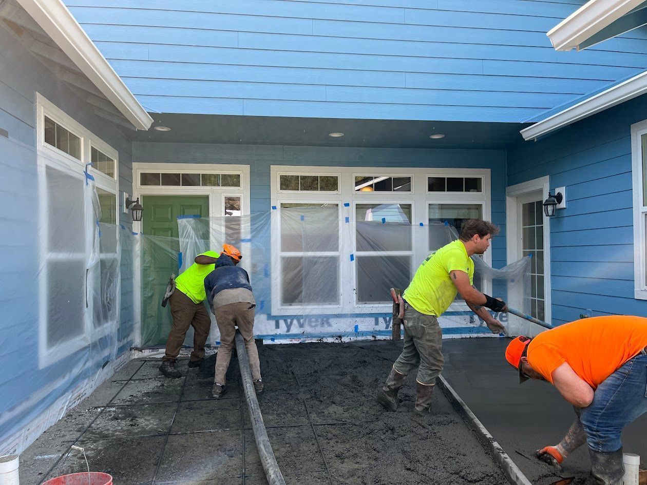 A group of construction workers are working on a concrete driveway in front of a house.