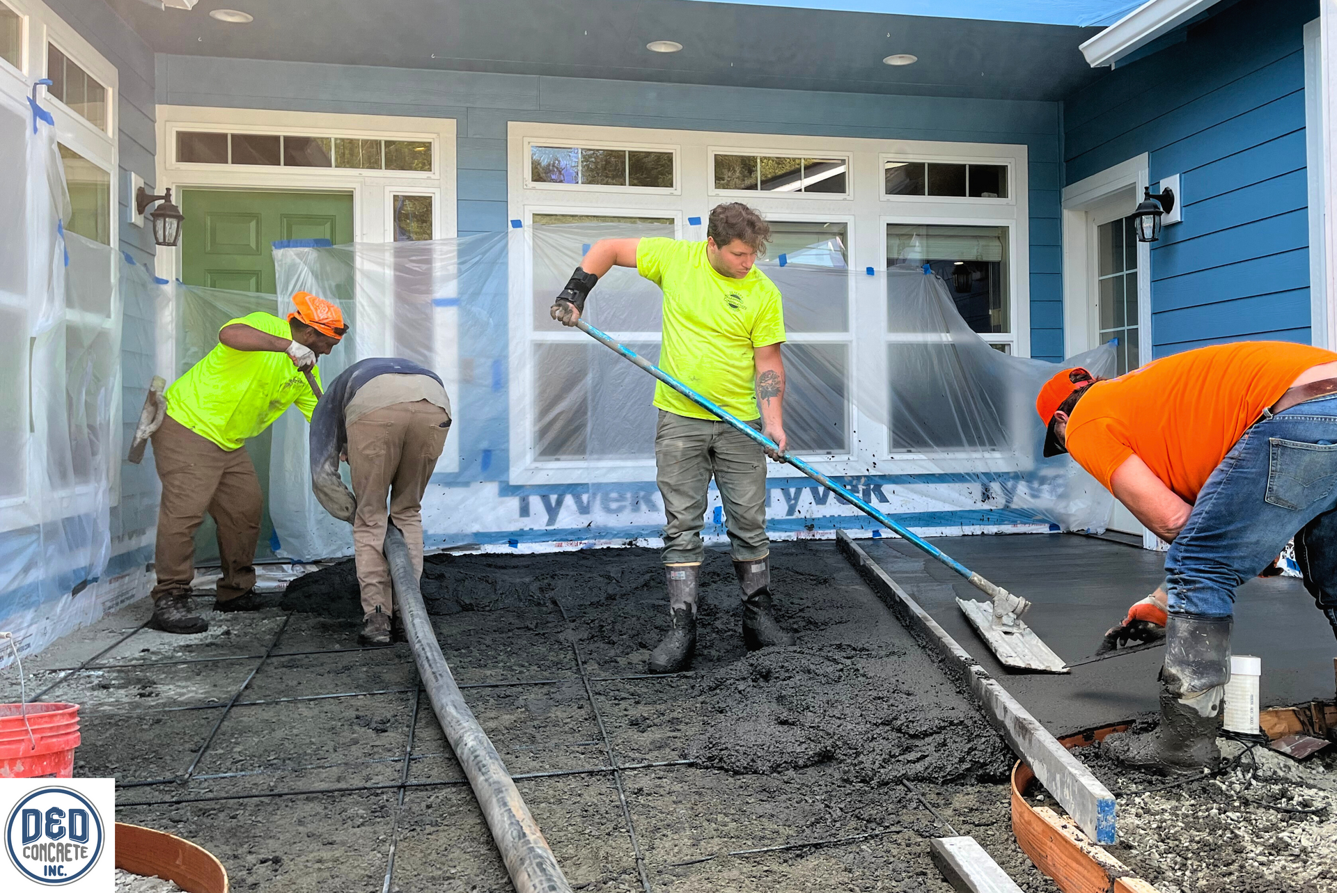 A group of construction workers are working on a concrete driveway in front of a house.