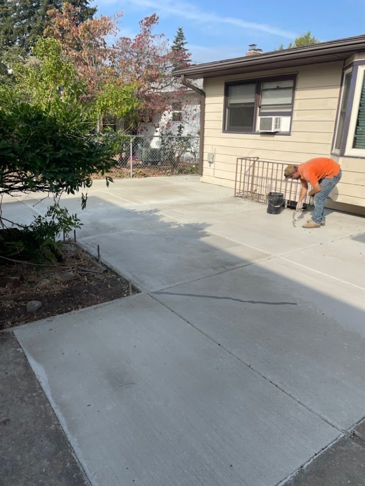A man is working on a concrete driveway in front of a house.