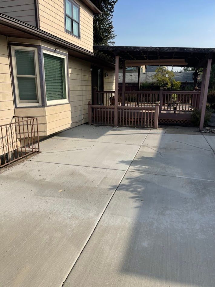 A concrete patio in front of a house with a pergola.