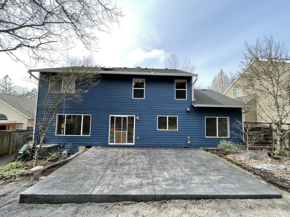 The back of a blue house with a concrete driveway in front of it.