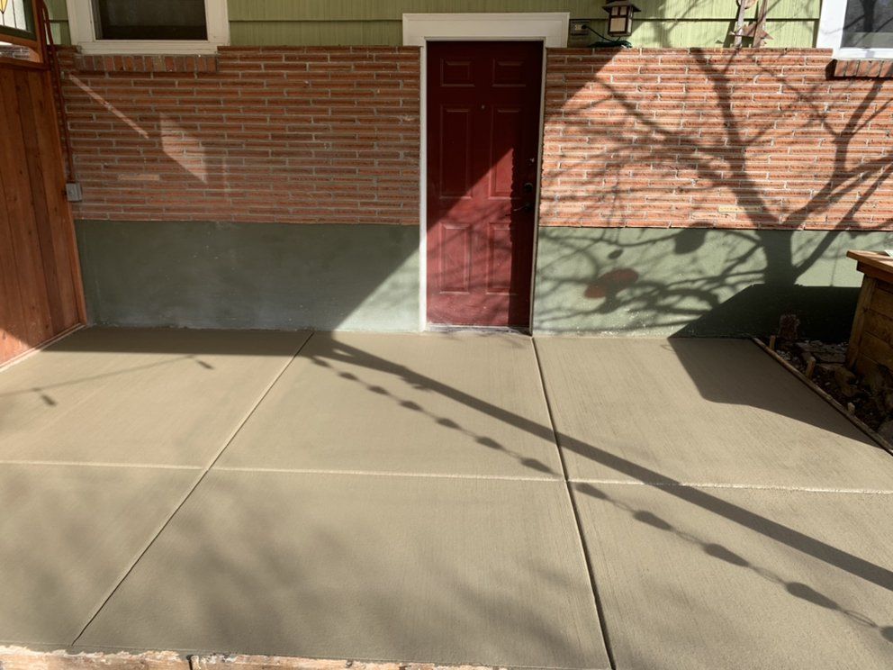 A concrete patio in front of a brick house with a red door.