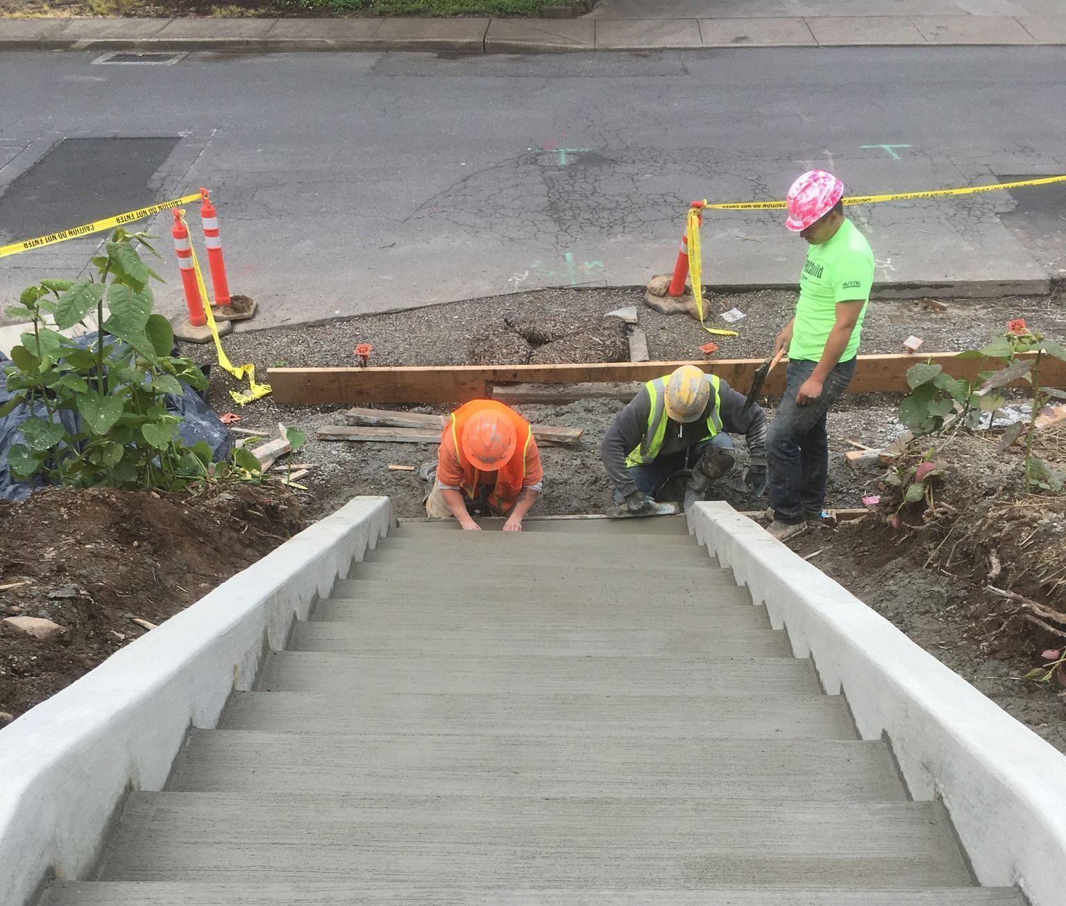 Three construction workers are working on a set of concrete stairs