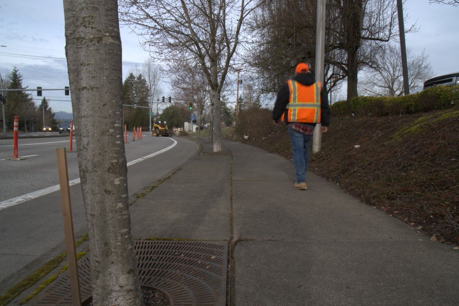 A man in an orange vest is walking down a sidewalk.