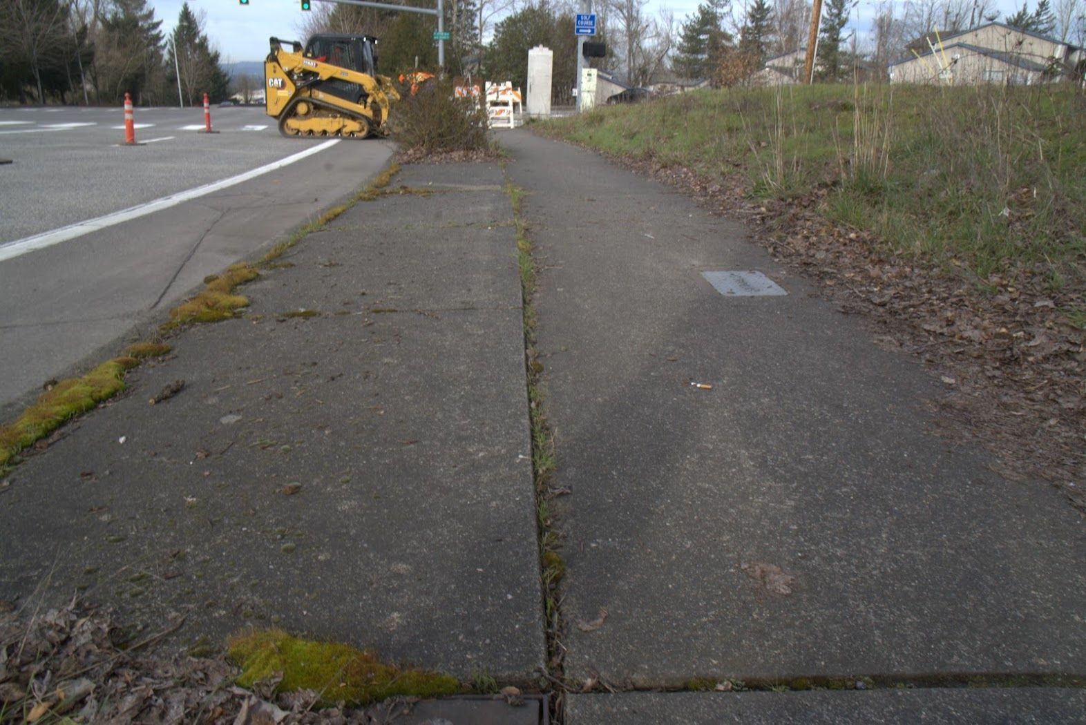 A yellow tractor is parked on the side of the road next to a sidewalk.