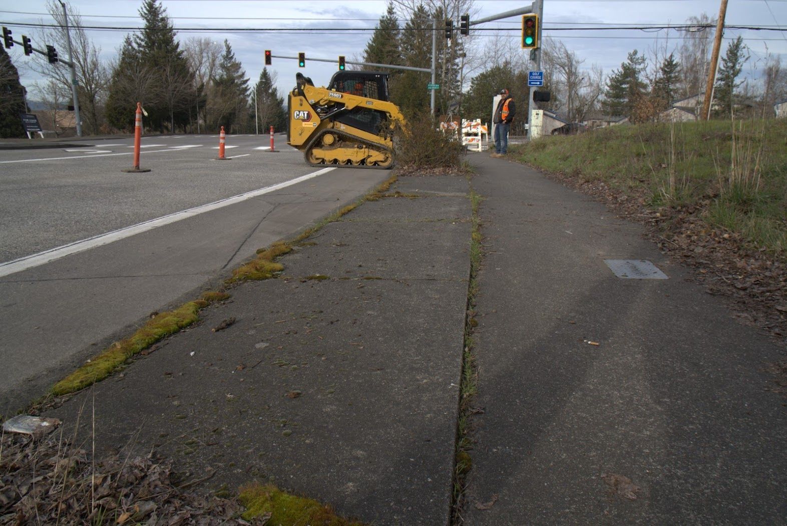 A yellow bulldozer is sitting on the sidewalk next to a street.