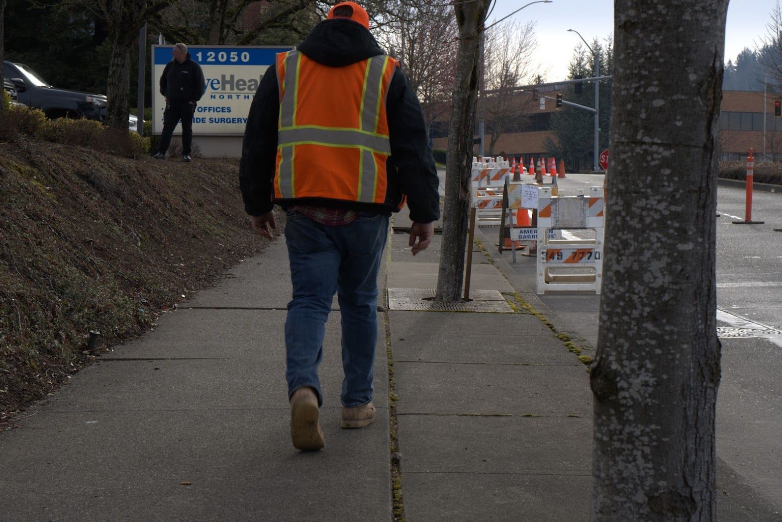 A man wearing an orange vest is walking down a sidewalk